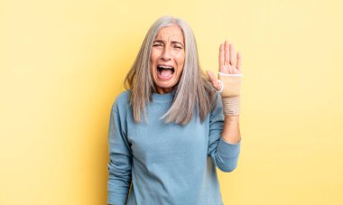 Orta yaşlı, güzel bir kadın agresif bir şekilde bağırıyor, çok kızgın görünüyor. el bandajı konsepti