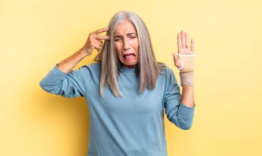 Orta yaşlı, güzel bir kadın mutsuz ve stresli görünüyor, intihar jesti silah işareti yapıyor. el bandajı konsepti