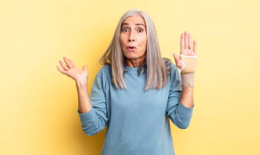 Orta yaşlı, güzel bir kadın şaşırmış ve şok olmuş görünüyor. Çenesi düşmüş ve elinde bir nesne var. el bandajı konsepti