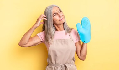 Orta yaşlı güzel bir kadın mutlu bir şekilde gülümsüyor ve hayal kuruyor ya da şüphe ediyor. fırın eldiveni kavramı