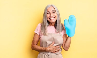 Orta yaşlı güzel bir kadın komik bir şakaya yüksek sesle gülüyor. fırın eldiveni kavramı