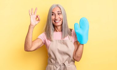 Orta yaşlı, güzel bir kadın kendini mutlu hissediyor, iyi bir jestle onaylıyor. fırın eldiveni kavramı