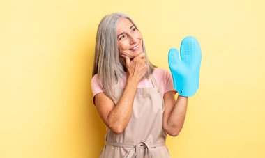 Orta yaşlı güzel bir kadın mutlu, kendinden emin ve elleri çenesinde gülümsüyor. fırın eldiveni kavramı