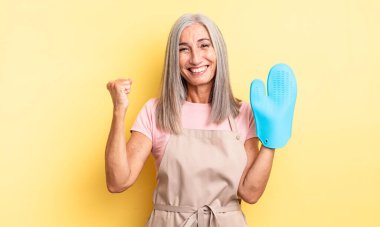 Orta yaşlı, güzel bir kadın şokta, gülüyor ve başarıyı kutluyor. fırın eldiveni kavramı