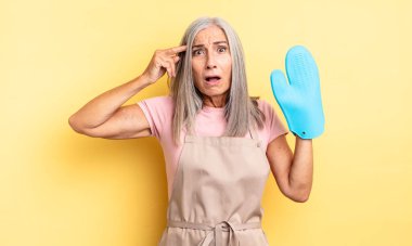 Orta yaşlı, güzel bir kadın mutlu, şaşkın ve şaşırmış görünüyor. fırın eldiveni kavramı