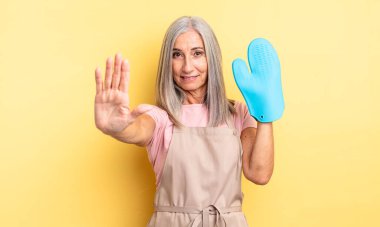 Orta yaşlı, güzel bir kadın ciddi görünüyor. Avuç içini gösteriyor. Durdurma hareketi yapıyor. fırın eldiveni kavramı