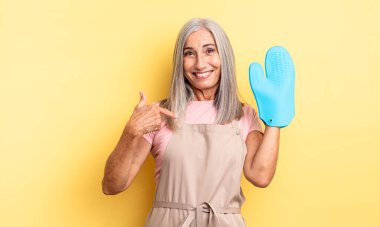 Orta yaşlı, güzel bir kadın kendini mutlu hissediyor ve heyecanla kendini işaret ediyor. fırın eldiveni kavramı