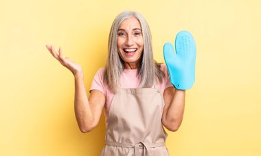 Orta yaşlı, güzel bir kadın inanılmaz bir şey karşısında mutlu ve şaşkın hissediyor. fırın eldiveni kavramı