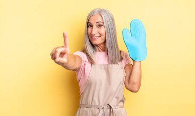 Orta yaşlı, güzel bir kadın gururla gülümsüyor ve kendinden emin bir numara oluyor. fırın eldiveni kavramı