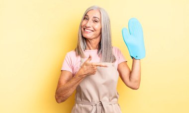 Orta yaşlı güzel bir kadın neşeli bir şekilde gülümsüyor, mutlu hissediyor ve bir tarafı işaret ediyor. fırın eldiveni kavramı