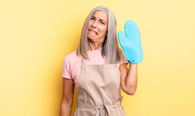 Orta yaşlı güzel bir kadın kafası karışmış ve şaşkın görünüyor. fırın eldiveni kavramı