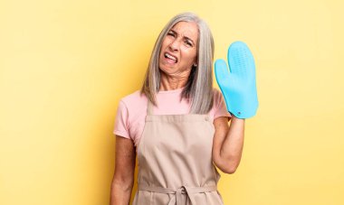 Orta yaşlı, güzel bir kadın şaşkın ve kafası karışık hissediyor. fırın eldiveni kavramı