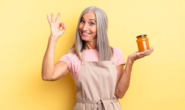 Orta yaşlı, güzel bir kadın kendini mutlu hissediyor, iyi bir jestle onaylıyor. Şeftali reçeli