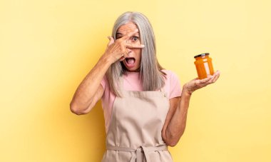 Orta yaşlı, güzel bir kadın şok olmuş, korkmuş ya da korkmuş görünüyor, yüzünü elleriyle kapatıyor. Şeftali reçeli