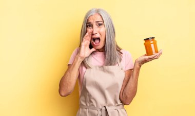 Orta yaşlı, güzel bir kadın kendini mutlu hissediyor. Elleri ağzının kenarında bağırıyor. Şeftali reçeli