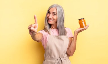 Orta yaşlı güzel bir kadın gülümsüyor ve arkadaş canlısı görünüyor. Bir numarayı gösteriyor. Şeftali reçeli