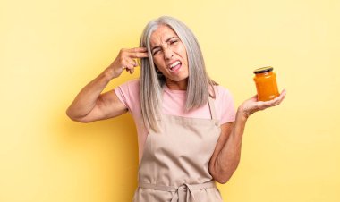 Orta yaşlı, güzel bir kadın mutsuz ve stresli görünüyor, intihar jesti silah işareti yapıyor. Şeftali reçeli