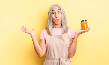 Orta yaşlı, güzel bir kadın şaşırmış ve şok olmuş görünüyor. Çenesi düşmüş ve elinde bir nesne var. Şeftali reçeli
