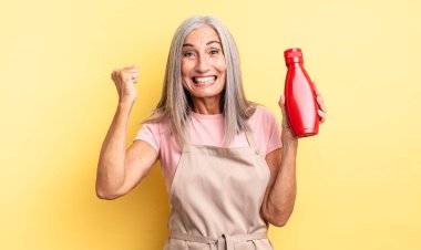 Orta yaşlı, güzel bir kadın şokta, gülüyor ve başarıyı kutluyor. Ketçap konsepti