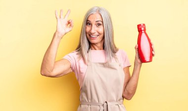 Orta yaşlı, güzel bir kadın kendini mutlu hissediyor, iyi bir jestle onaylıyor. Ketçap konsepti