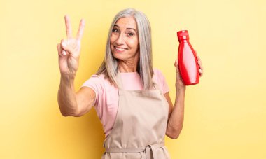 Orta yaşlı güzel bir kadın gülümsüyor ve mutlu görünüyor, zafer ya da barış işareti yapıyor. Ketçap konsepti