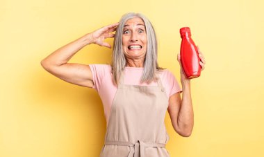 Orta yaşlı, güzel bir kadın stresli, endişeli ya da korkmuş, elleri başının üstünde. Ketçap konsepti