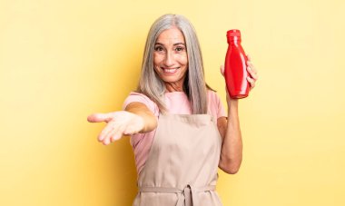 Orta yaşlı, güzel bir kadın arkadaşça gülümsüyor ve bir konsept sunuyor. Ketçap konsepti