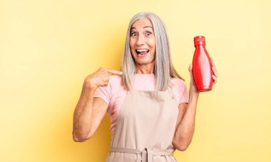 Orta yaşlı, güzel bir kadın kendini mutlu hissediyor ve heyecanla kendini işaret ediyor. Ketçap konsepti