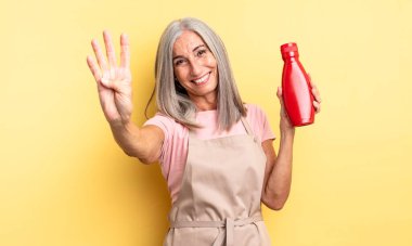 Orta yaşlı güzel bir kadın gülümsüyor ve arkadaş canlısı görünüyor, dört numarayı gösteriyor. Ketçap konsepti