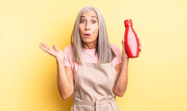 Orta yaşlı, güzel bir kadın şaşırmış ve şok olmuş görünüyor. Çenesi düşmüş ve elinde bir nesne var. Ketçap konsepti