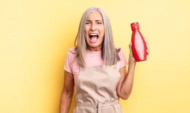 Orta yaşlı, güzel bir kadın agresif bir şekilde bağırıyor, çok kızgın görünüyor. Ketçap konsepti