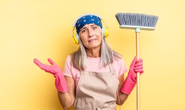 Orta yaşlı, güzel bir kadın şaşkın, şaşkın ve şüpheci hissediyor. ev ve süpürge kavramı