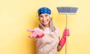 Orta yaşlı, güzel bir kadın arkadaşça gülümsüyor ve bir konsept sunuyor. ev ve süpürge kavramı