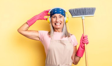 Orta yaşlı, güzel bir kadın stresli, endişeli ya da korkmuş, elleri başının üstünde. ev ve süpürge kavramı