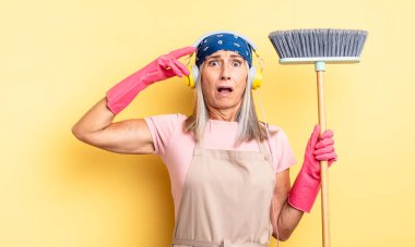 Orta yaşlı, güzel bir kadın mutlu, şaşkın ve şaşırmış görünüyor. ev ve süpürge kavramı