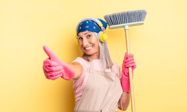 Orta yaşlı, güzel bir kadın gururlu, olumlu gülümsüyor. ev ve süpürge kavramı