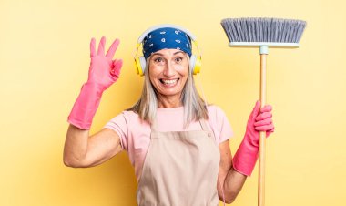 Orta yaşlı, güzel bir kadın kendini mutlu hissediyor, iyi bir jestle onaylıyor. ev ve süpürge kavramı