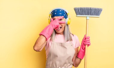 Orta yaşlı, güzel bir kadın şok olmuş, korkmuş ya da korkmuş görünüyor, yüzünü elleriyle kapatıyor. ev ve süpürge kavramı