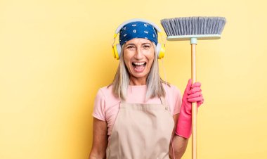 Orta yaşlı, neşeli ve asi tavırları olan, şaka yapan ve dilini dışarı çıkaran güzel bir kadın. ev ve süpürge kavramı