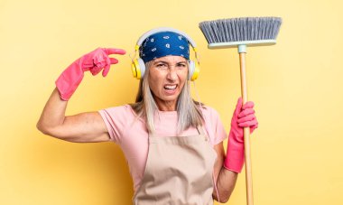 Orta yaşlı güzel bir kadın kafası karışık ve şaşkın hissediyor, deli olduğunu gösteriyor. ev ve süpürge kavramı