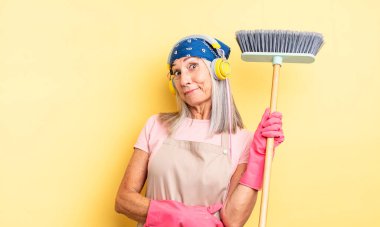 Orta yaşlı güzel bir kadın omuz silkiyor, kafası karışık ve kararsız. ev ve süpürge kavramı