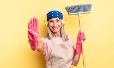 Orta yaşlı güzel bir kadın gülümsüyor ve arkadaş canlısı görünüyor, dört numarayı gösteriyor. ev ve süpürge kavramı