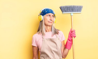 Orta yaşlı, güzel bir kadın üzgün, üzgün ya da kızgın ve yana bakıyor. ev ve süpürge kavramı