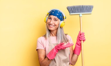 Orta yaşlı güzel bir kadın neşeli bir şekilde gülümsüyor, mutlu hissediyor ve bir konsept gösteriyor. ev ve süpürge kavramı