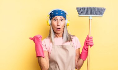 Orta yaşlı, güzel bir kadın inançsızlıktan şaşkın şaşkın bakıyor. ev ve süpürge kavramı