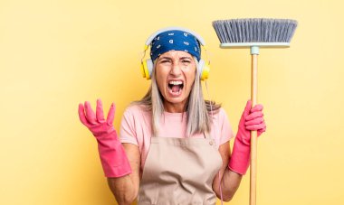 Orta yaşlı, güzel bir kadın sinirli, sinirli ve sinirli görünüyor. ev ve süpürge kavramı