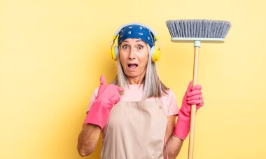 Orta yaşlı güzel bir kadın şok olmuş ve ağzı açık, kendini işaret eden bir şekilde şaşırmış görünüyor. ev ve süpürge kavramı