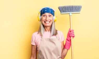 Orta yaşlı, güzel bir kadın mutlu ve hoş bir şekilde şaşırmış görünüyor. ev ve süpürge kavramı