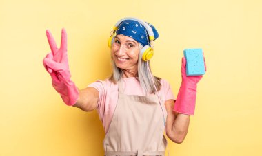 Orta yaşlı güzel bir kadın gülümsüyor ve mutlu görünüyor, zafer ya da barış işareti yapıyor. Temizleyici.