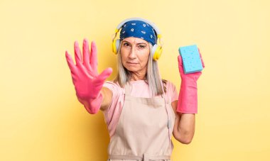 Orta yaşlı, güzel bir kadın ciddi görünüyor. Avuç içini gösteriyor. Durdurma hareketi yapıyor. Temizleyici.